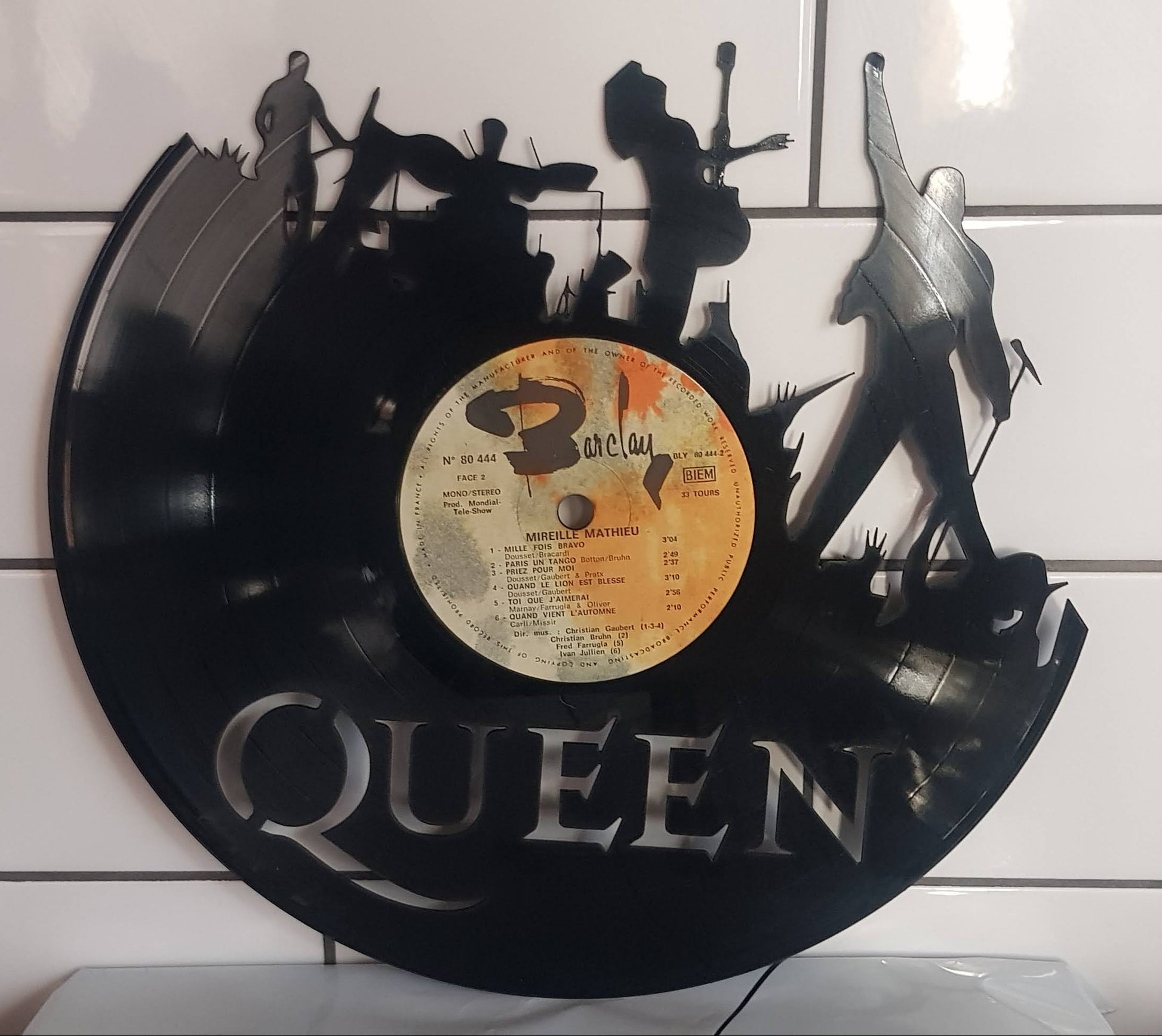 Vinyl record wall art with 'Queen' band members on a white tiled wall.